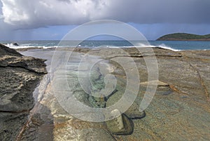 Tide pool on rocky Caribbean shore with rain at sea