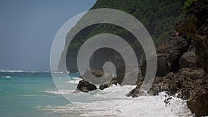 Tide waves with foam and splashes are crushing beach with stones and rock in sunny day in ocean on tropic beach. Water