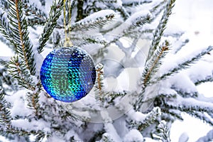 Tidewater green Christmas ball hangs on a snow-covered branch of a Christmas tree. Blue light bokeh background. New Year