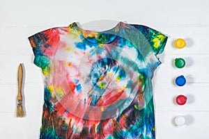 Tie dye t-shirt with brush and paint on a white table. Flat lay.