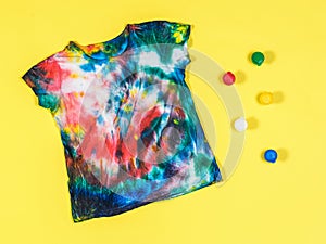 Tie dye t-shirt and colorful paint cans on a yellow background. Flat lay.