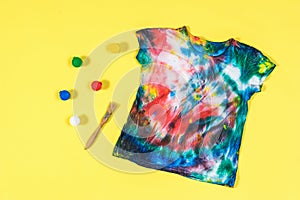 Tie dye t-shirt with scattered colors on a yellow background. Flat lay.