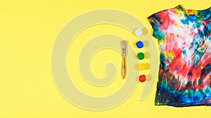 Tie dye t-shirt with scattered colors on a yellow background. Flat lay. Place for text.