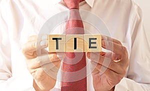 Tie word on wooden cubes in hands of man in white shirt and red tie close up