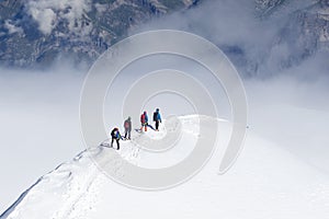 Tied climbers climbing mountain with snow field tied with a rope with ice axes and helmets