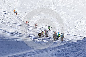 Tied climbers climbing mountain with snow field tied with a rope with ice axes and helmets