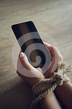 Tied female hands are holding a mobile phone. Mobile phone addic