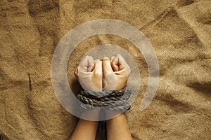 tied female hands by an old rope on brown cloth, tied hands