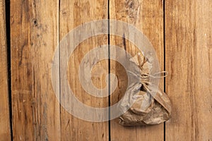 Tied paper bag against a wooden background. Brown paper bag tied with string. Rough cracked boards. Copy space for text and design