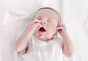 Tiered baby lying down on white sheets yawning.