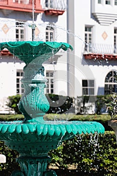 Tiered verdigris metal fountain with spraying water and white and terra-cotta building in background photo