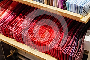 Ties of red shade and warm tones with strict design pattern are folded in row in the window of fashionable mens clothing store