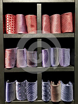 Ties, from red to purple, are folded into rolls on display shelves.