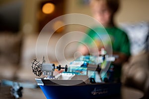 Tiffin, Iowa, USA - 9.2021 - Focus on Lego ship construction set with blurred child in the background playing
