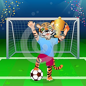 A tiger in uniform standing on the ball and cheering with goblet on the soccer field