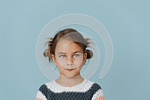 Tight-lipped little girl in striped sweater, hair in buns over blue background.