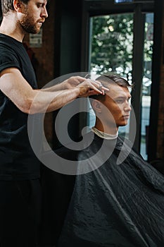 Tight-lipped male hairdresser making a haircut for a young man in a barber shop