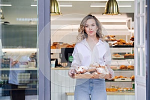 Tight lipped woman posing with a tray full of pastry in a doorstep of her shop