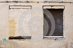 A blocked window and a window closed with a roller shutter in the old wall of the building