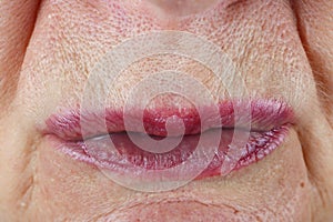 Tightly squeezed narrow pink lips of an elderly woman. The pores and skin defects are clearly visible