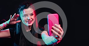 Tik tok advertisement concept. Young girl posing with smart phone in her hands, making selfie on black background. TIK TOK is a