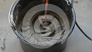 Tile adhesive is mixed using an electric drill in a bucket.