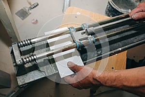 Tile cutter in the man`s hand. A builder is cutting white tiles for renovation maintenance work indoors