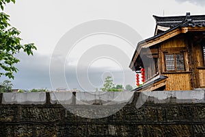 Tile-roofed timberwork building behind stone wall after rain in