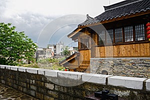 Tile-roofed timberwork building outside stone wall in cloudy spring after rain