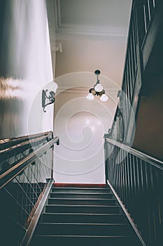 Tiled 1950's style public house stairwell indoors with a minimalistic chandelier on the roof