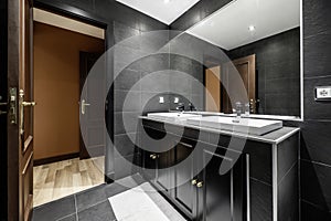 Tiled bathroom with black slate tiles, individual white porcelain sinks on black cabinet with mirror built into the wall