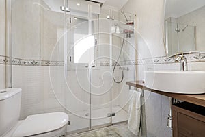 Tiled bathroom with white tiles, shower cabin with glass screens and circular porcelain sink with mirror on the wall