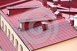 Tiled red metal roof with chimneys and windows