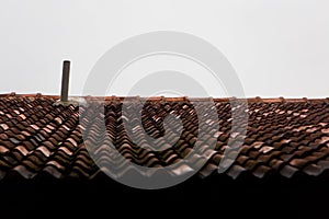 Tiled roof and chimney against the background of an uninformative cloudy sky