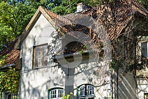 Tiled roof of an old house from the 19th century. Wooden windows without restoration on the facade of a cottage in the forest