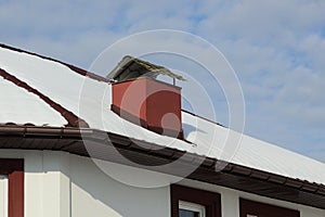 Tiled roof of a private house under white snow with a red metal chimney on a winter street