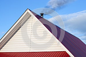 Tiled roof top with chimney with blue cloudy sky in background. Smoke raising from a chimney