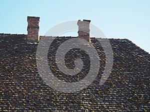 Tiled roof with twin tailpipes. Old tiles with moss and lichens on the roof of a residential building. Heating buildings