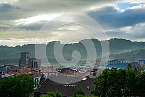 Tiled roofs of an old Spanish town against background of green hills in dawn fog. View of the tower of St. Peter the Apostole