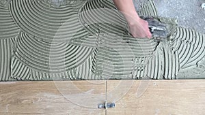 A tiler applies adhesive to the floor to install ceramic tiles. Laying tiles at a construction site. Selective focus, plenty of