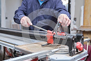 Tiler hands cutting a ceramic wood effect tile with a manual tile cutter.