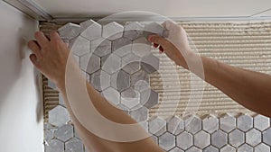 A tiler installs spacers between ceramic tiles. Gray tiles - mosaic in the kitchen. A tiler is gluing mosaic tiles to a