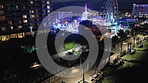tilt aerial footage of people sitting in brown wooden swings along the boardwalk and amusement park rides with colorful lights