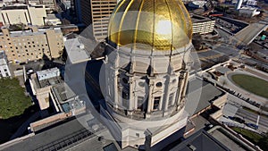 Tilt aerial shot of the Georgia Capitol Museum surrounded by skyscrapers and office buildings with cars driving on the freeway