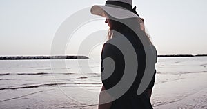 Tilt down on back lit young beautiful woman in summer hat meditating at incredible calm sunrise sea beach slow motion.