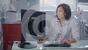 Tilt down of professional female doctor in lab coat typing on futuristic computer with transparent monitor at