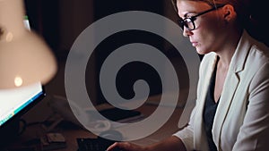 Tilt-down shot of pretty young business woman working on computer late at night typing using keyboard sitting at desk