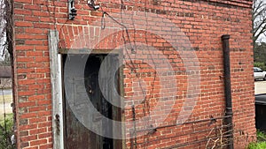 Tilt of an old overgrown red brick single jail unit open iron door with lock