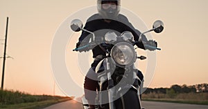 Tilt shot: Biker in a black jacket rides on the neck at sunset