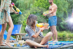 Tilt shot of cheerful couples enjoying with squirt guns on pier during summer